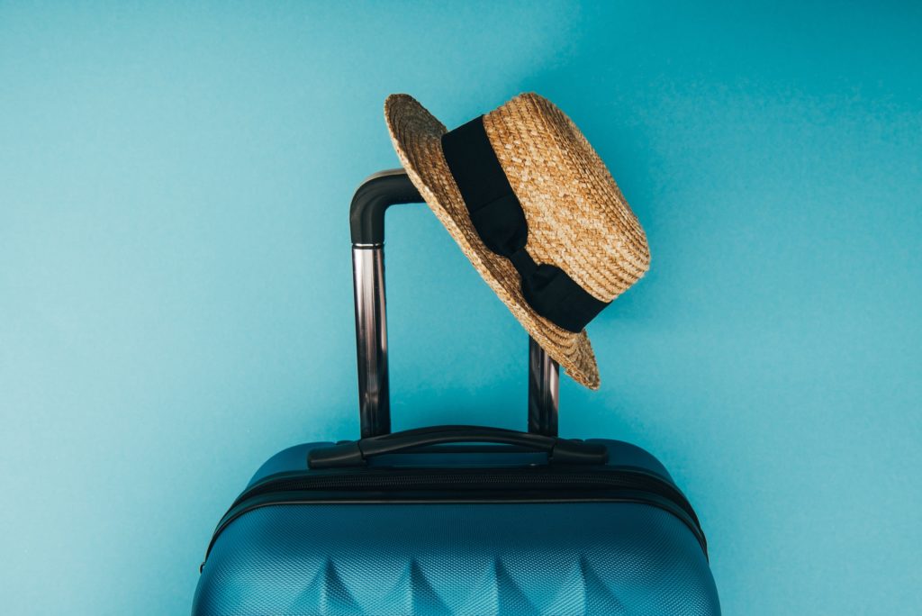 top view of straw hat and travel bag on blue background